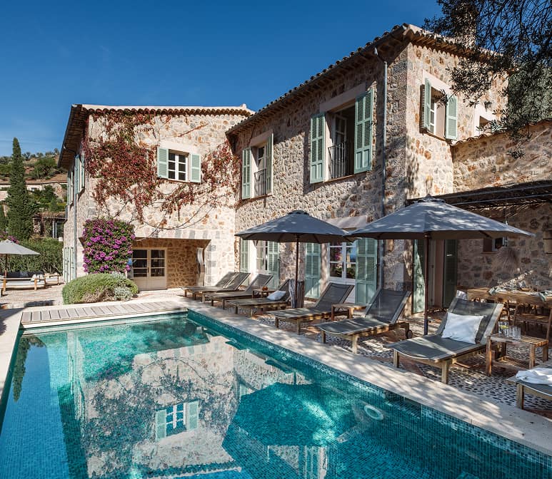 Mediterranean stone villa with private swimming pool, sun loungers and traditional shuttered windows under clear blue sky