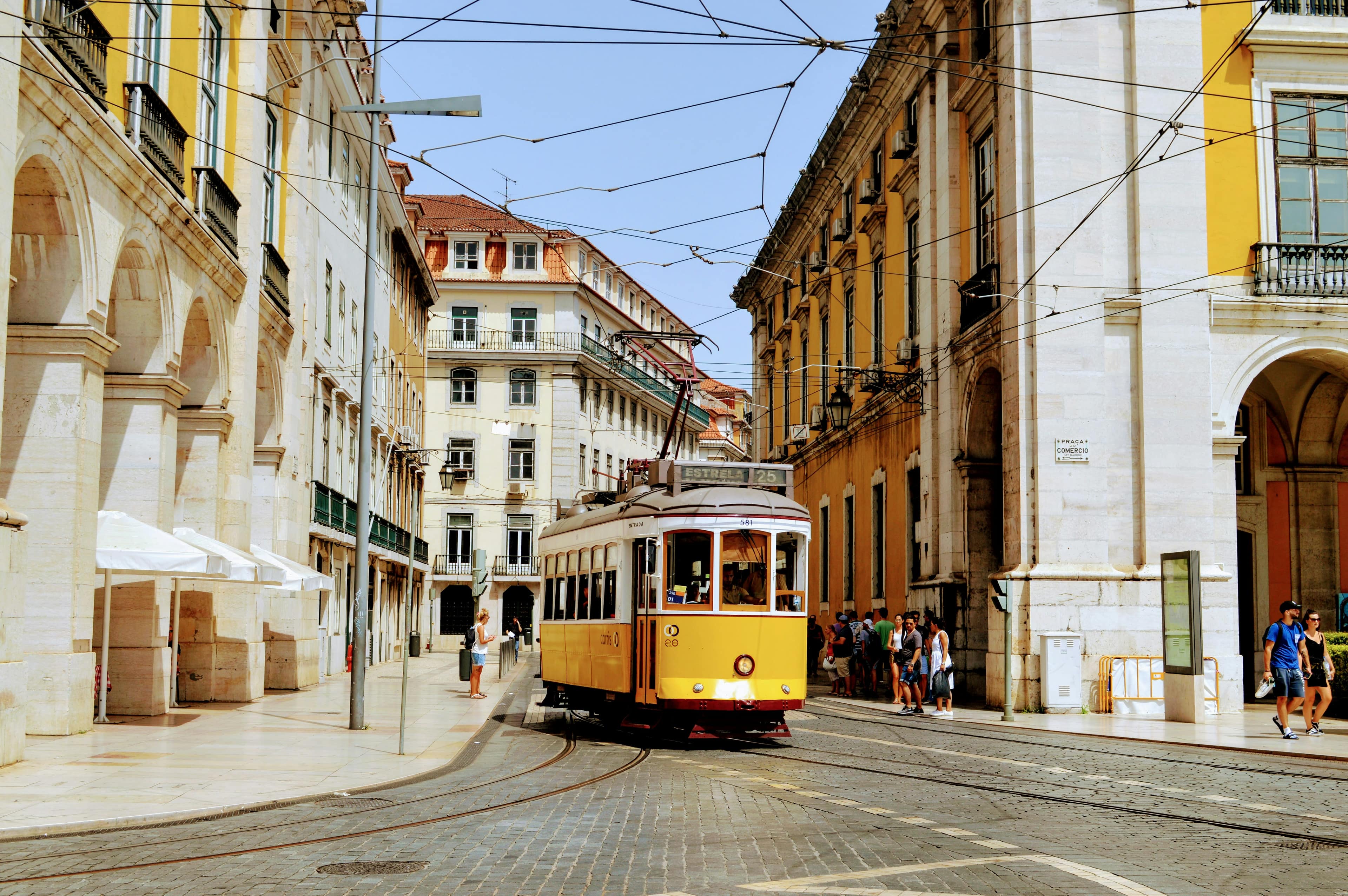 Iconic yellow tram 25 rounding a cobbled corner near Praça do Comércio in Lisbon's historic city centre on a sunny day