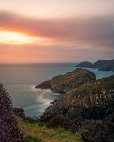 Dramatic sunset over the Pembrokeshire coastline with rugged cliffs, turquoise sea, and heather-covered headlands