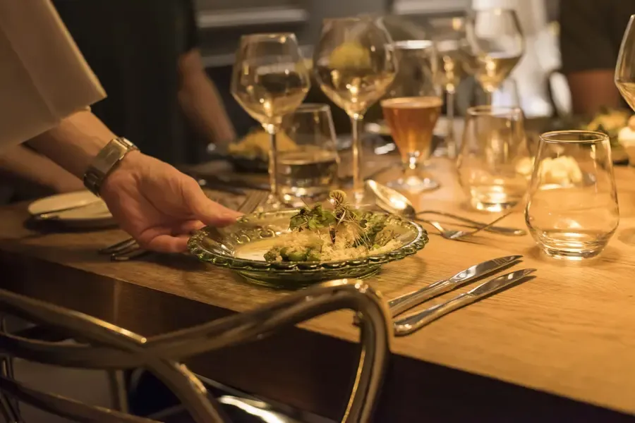 Fine dining experience with gourmet dish being served at candlelit table with wine glasses in luxury chalet