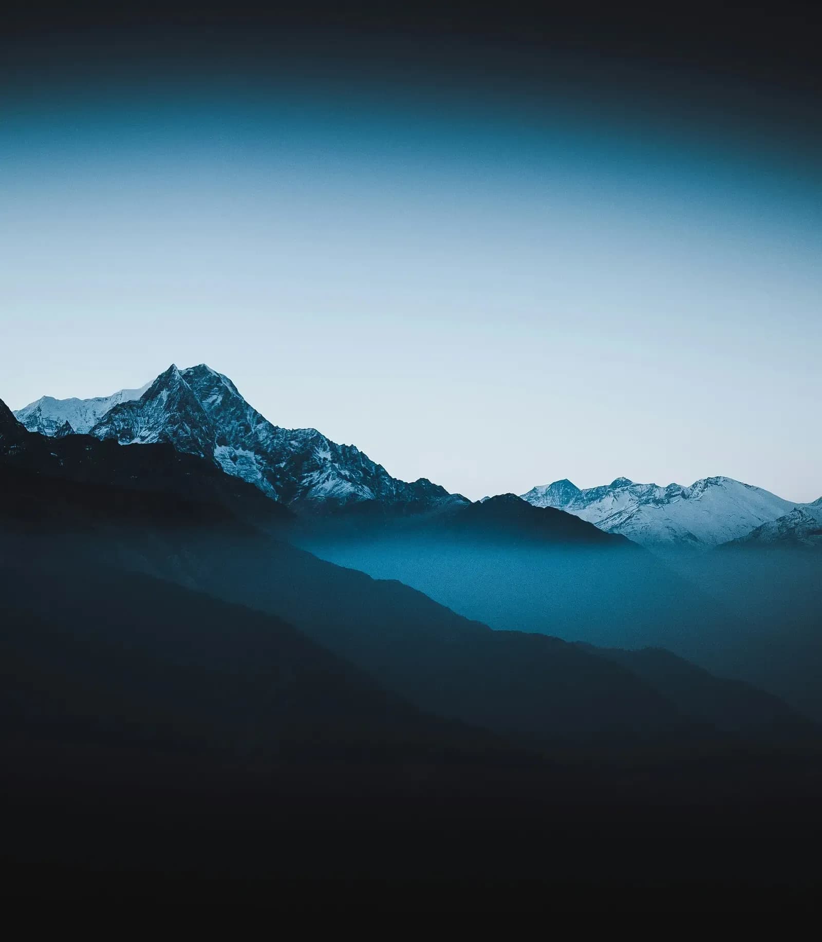 Snow-capped mountain peaks rising through misty blue valleys at dawn, showcasing dramatic alpine scenery near luxury ski cha…