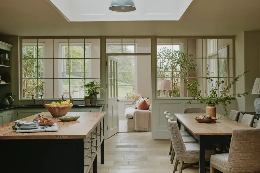 Open-plan kitchen diner in a luxury holiday cottage with sage green cabinetry, solid wood island, and crittall-style windows…