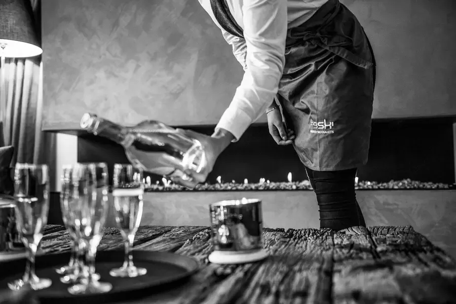 Professional drinks service with champagne being poured into glasses on rustic wooden table in luxury chalet