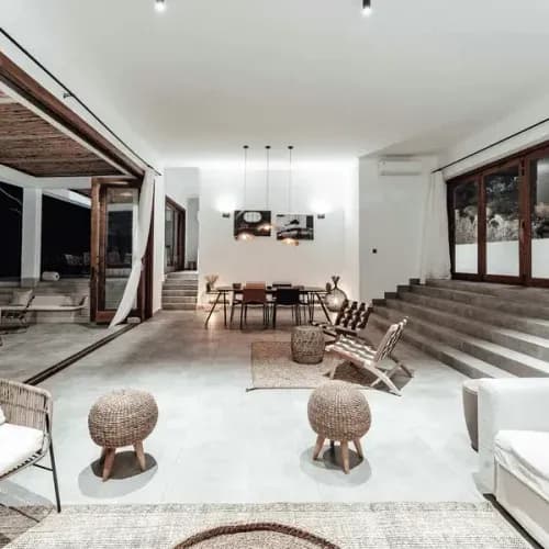 Modern open-plan living space with polished concrete floors, exposed timber beams, and woven furniture overlooking outdoor t…