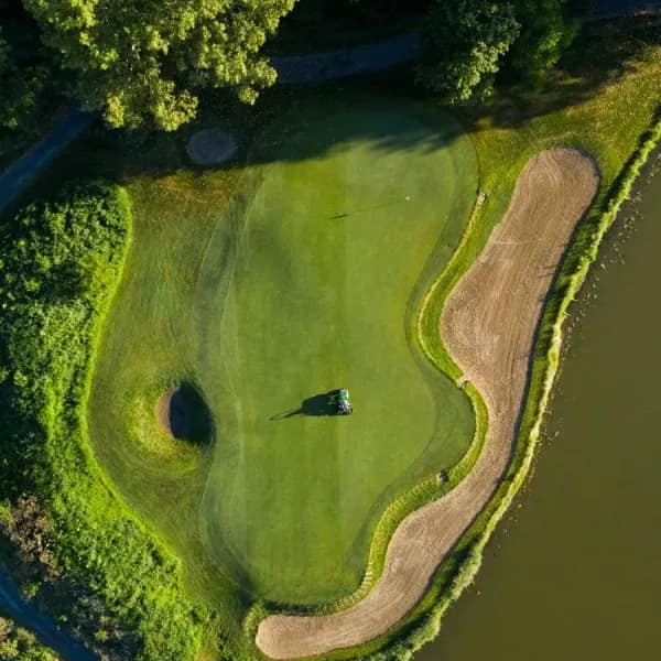 Aerial view of pristine golf green with sand bunker and wooded surroundings at luxury countryside estate