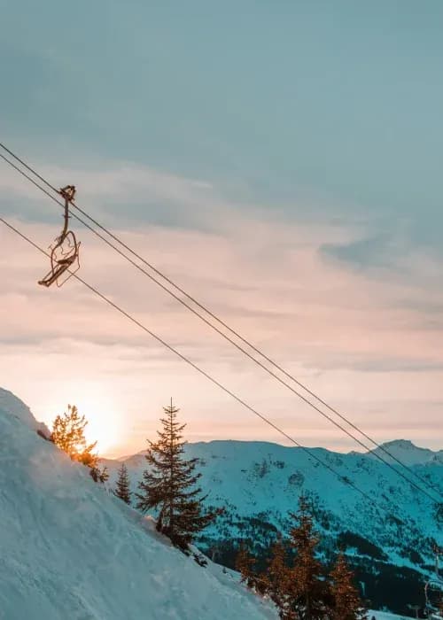 Chairlift ascending snowy mountain slopes at sunset with pink and blue alpine sky, perfect for luxury ski chalet holidays