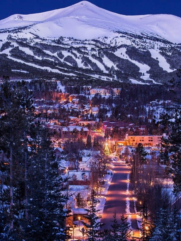 Snow-covered ski resort town at twilight with illuminated chalets nestled below mountain slopes and ski runs